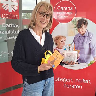 khg-Mitarbeiterin Daniela Ramb steht vor dem Eingang Caritas-Sozialstation Göttingen / Gleichen und hält eine Karte und ein Osternest in ihren Händen.