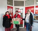 Tabea Below (l.) und Daniela Ramb (r.) aus der khg übergeben die gepackten Plätzchentüten vor der Sozialstation an Christiane Koch von der Caritas. 